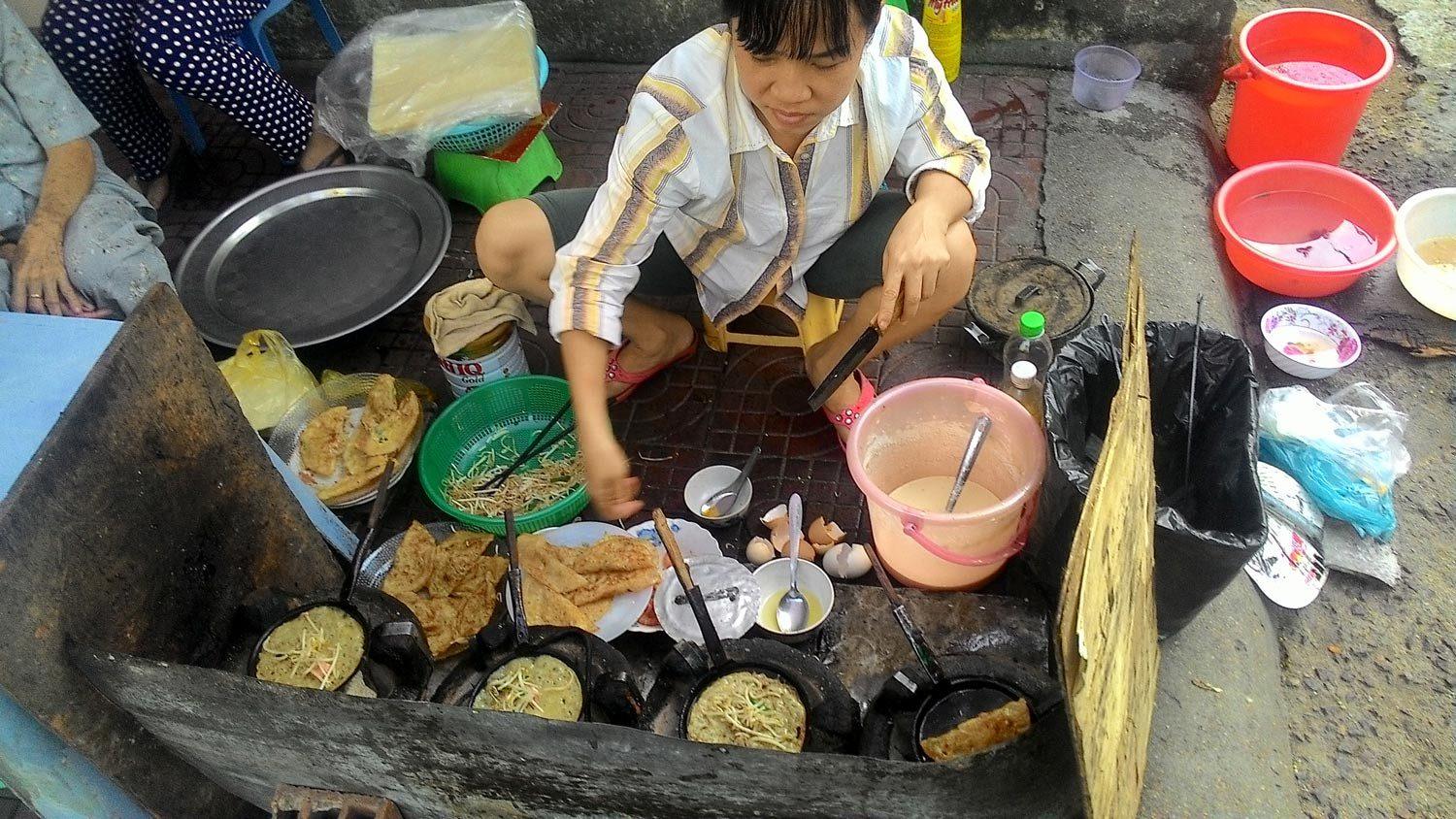 A street vendor cooking banh xeo pancakes over an open flame