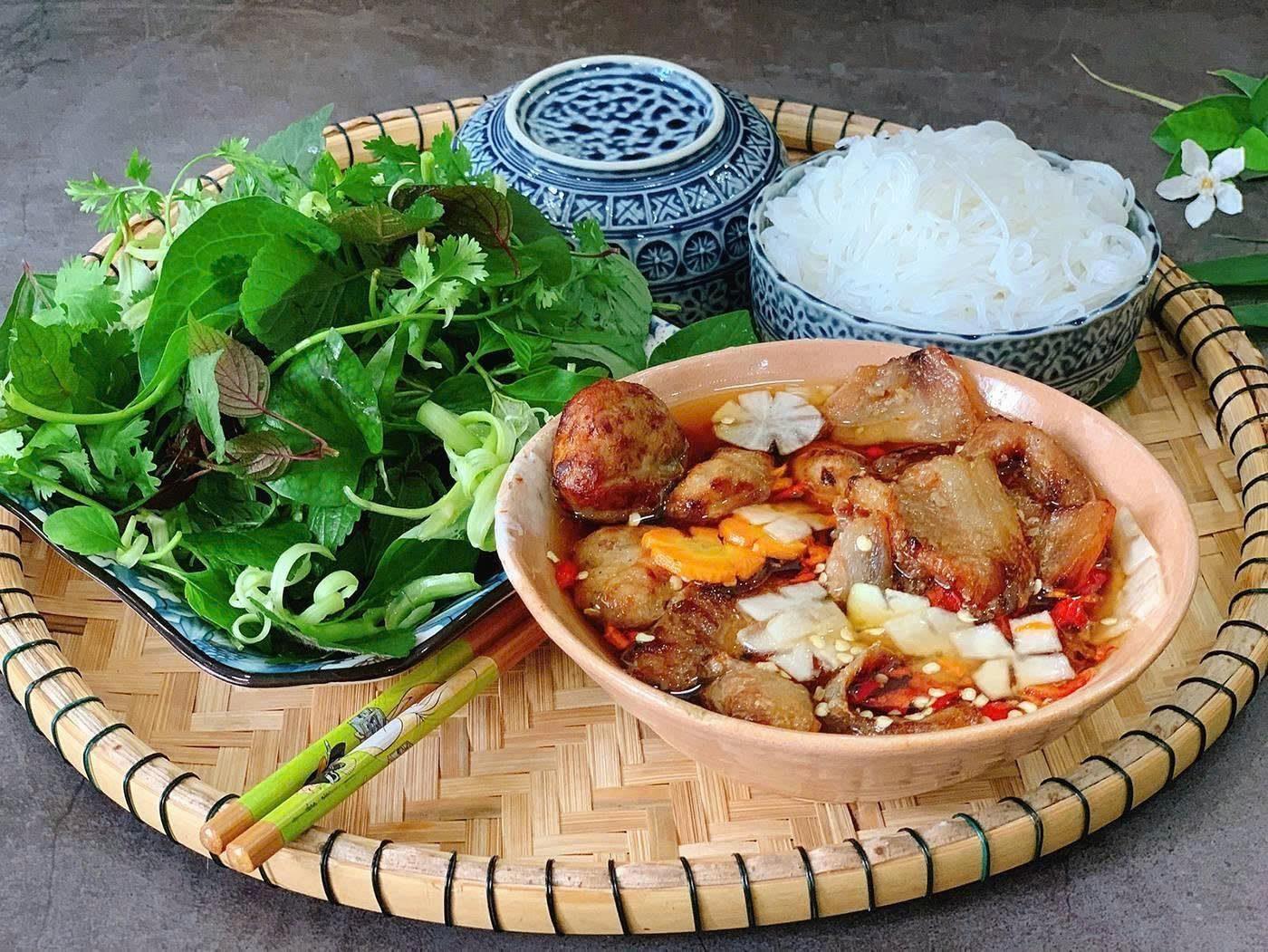 A close-up bowl of bun cha dipping broth with grilled pork and herbs, Hanoi