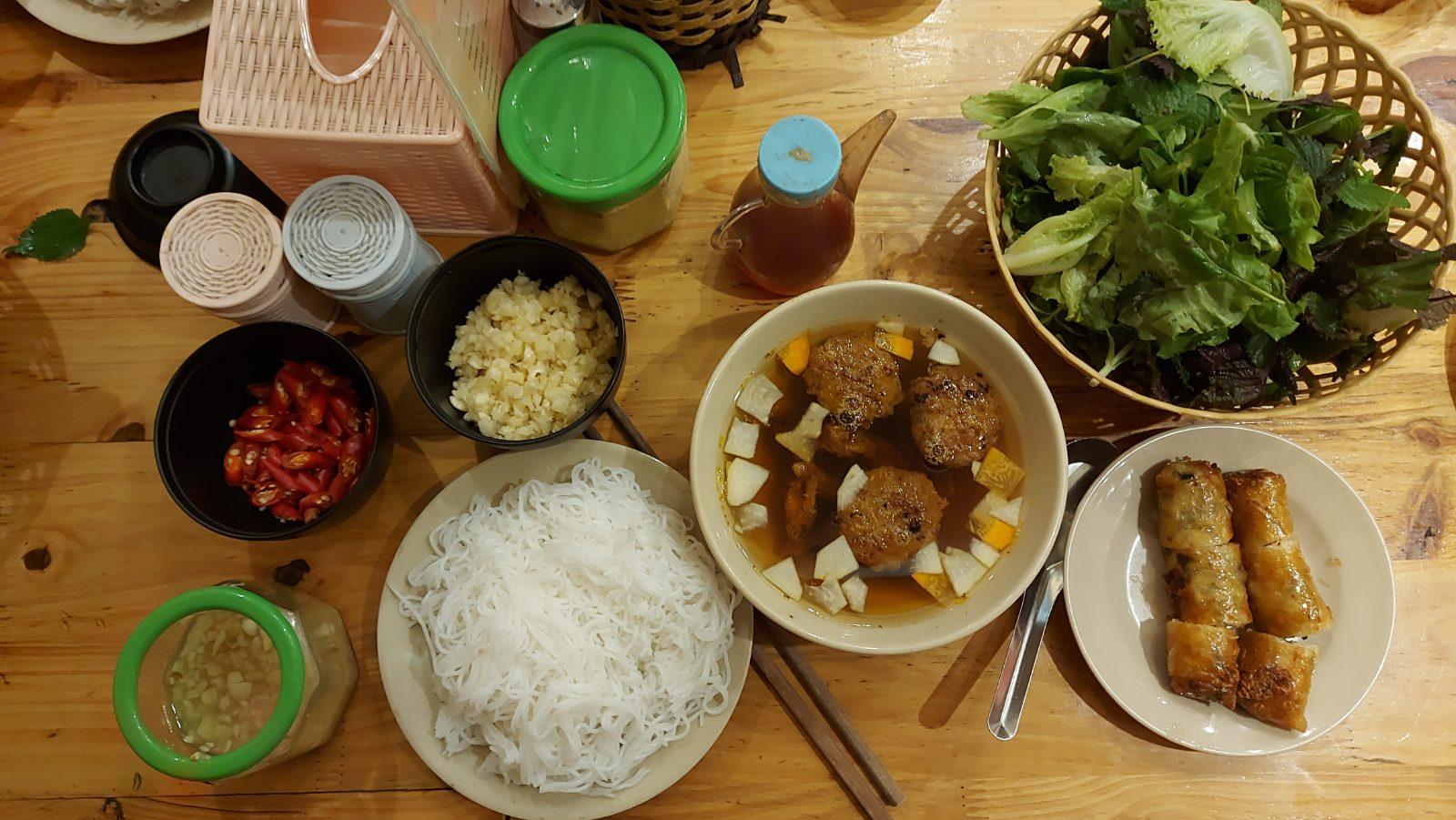 A full bun cha table setting with dipping broth, rice vermicelli, herbs, and fried spring rolls, Hanoi