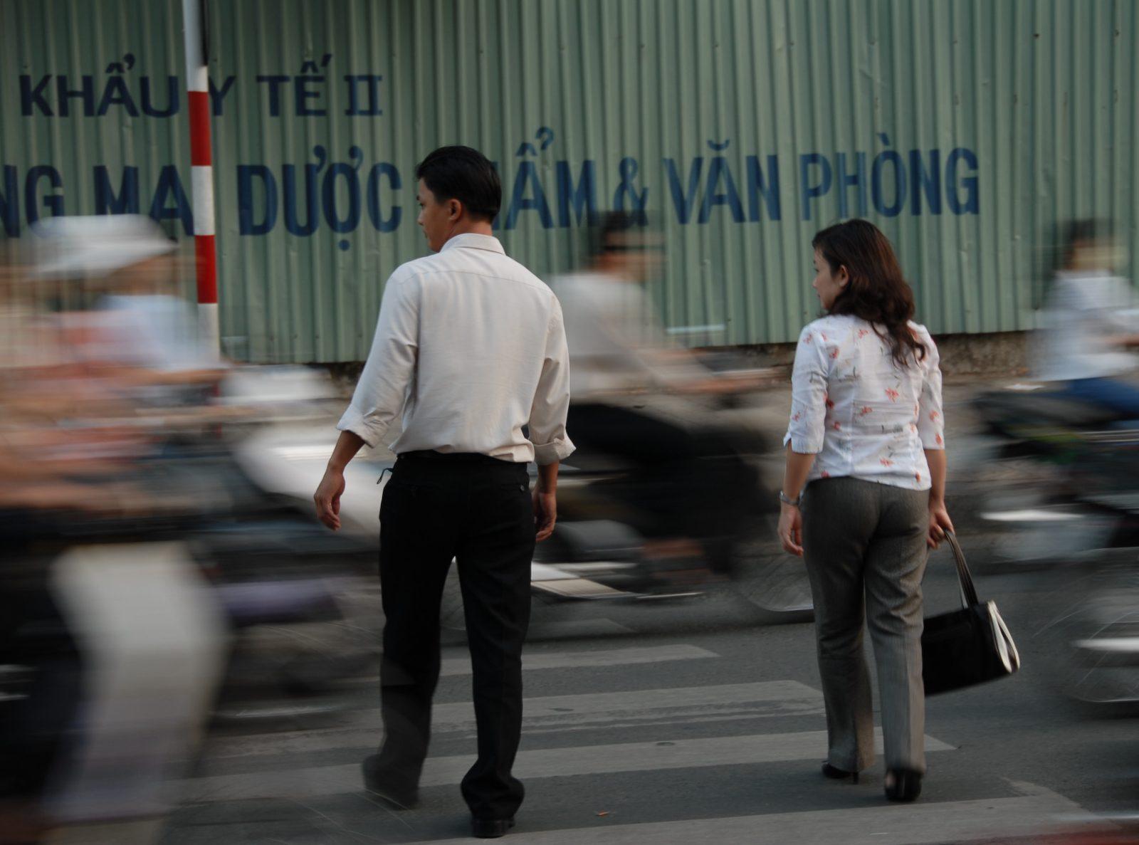 A pedestrian crossing a busy street in Ho Chi Minh City amid motorbike traffic