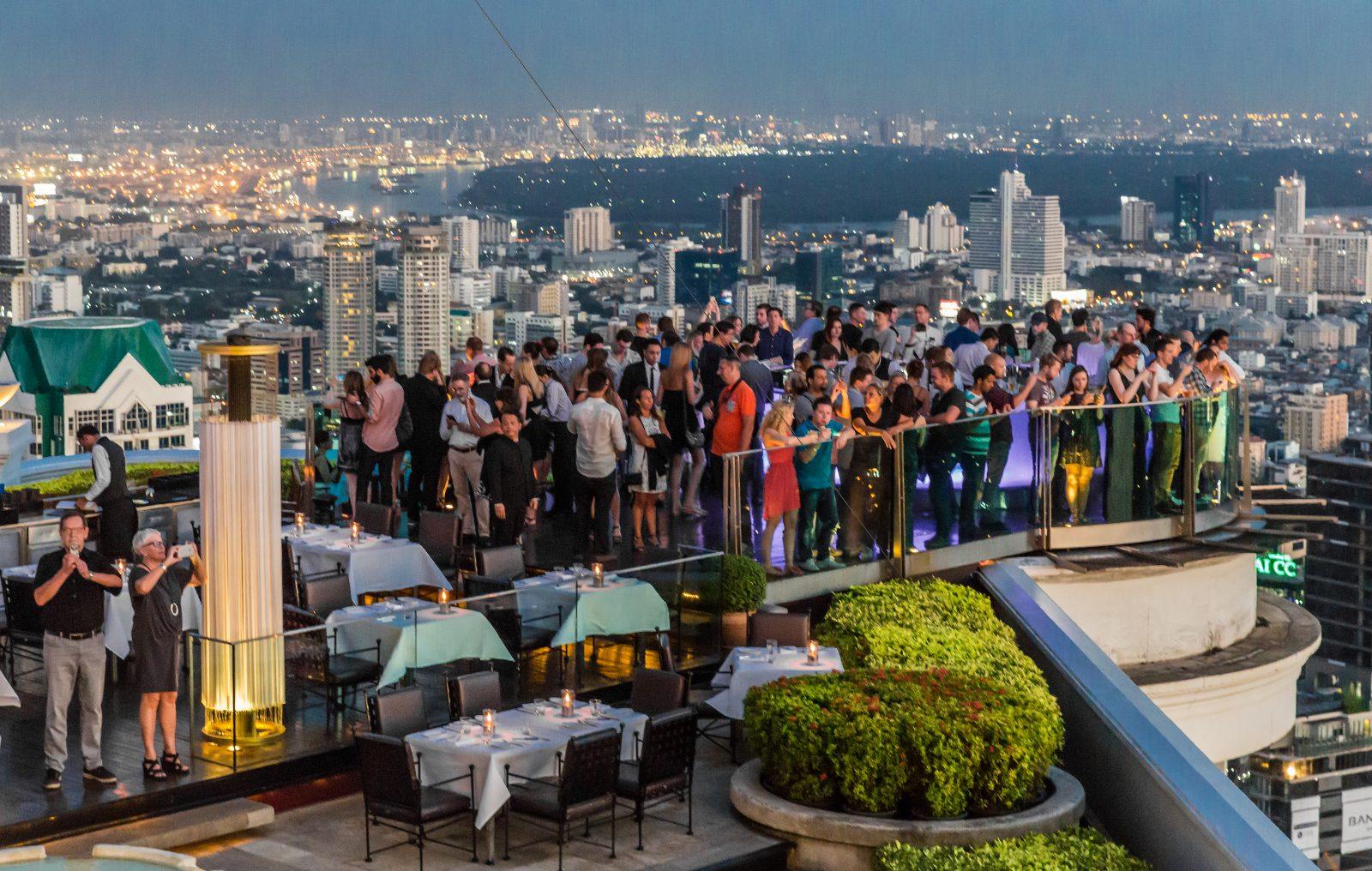 A rooftop sky bar in Bangkok lit up at night with skyline views