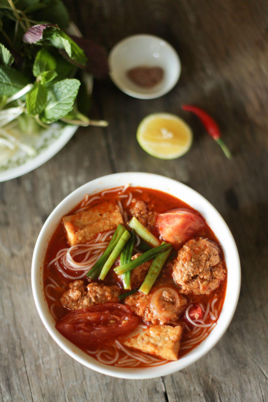 Close-up bowl of bun rieu with tomato, tofu, and crab paste cakes