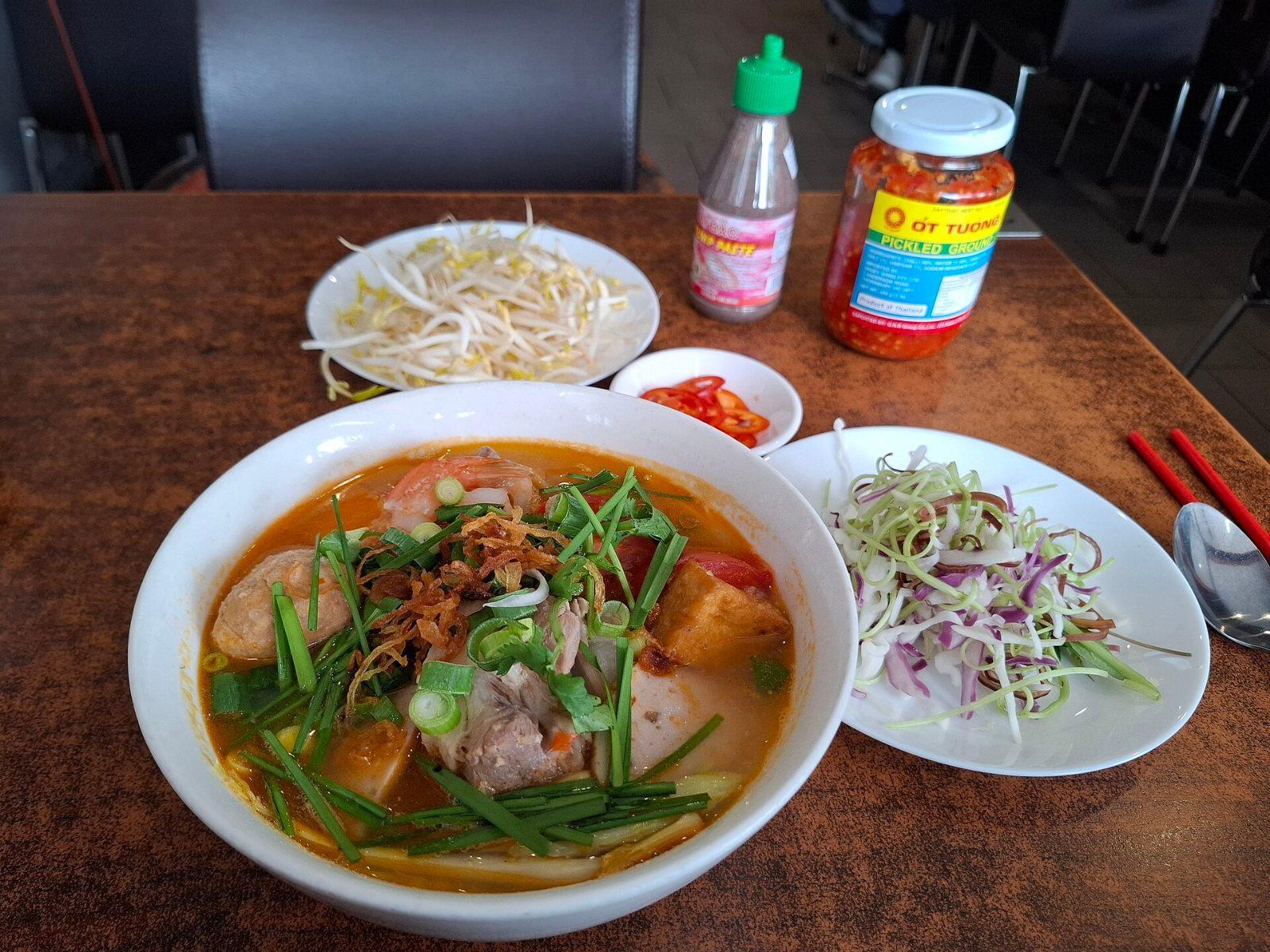 A bowl of bun rieu, Vietnamese crab and tomato noodle soup, served with fresh herbs and vegetables