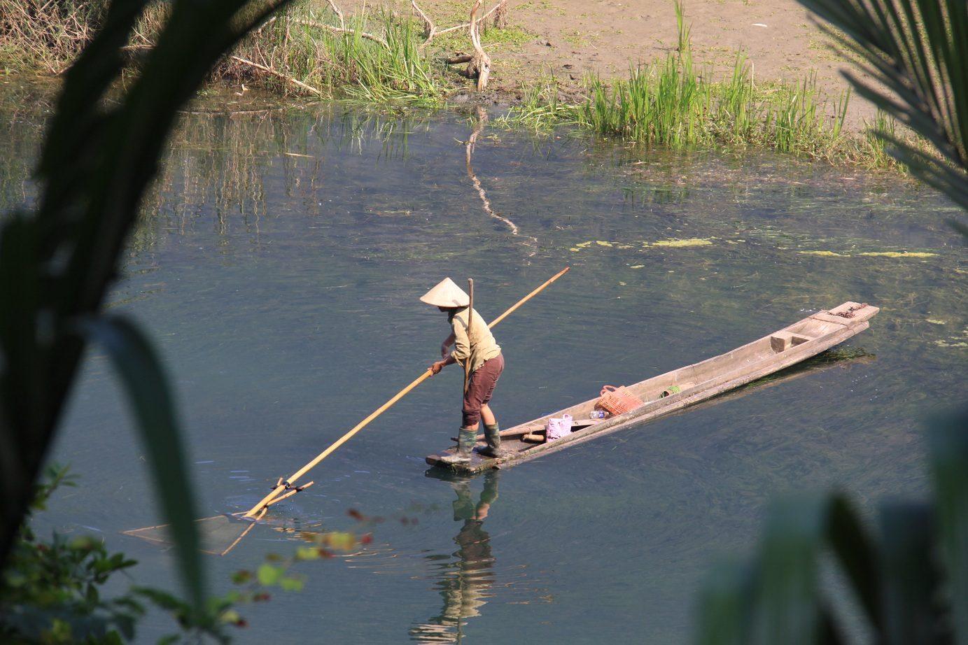 A local resident poling a traditional wooden dugout boat near Ba Be Lake