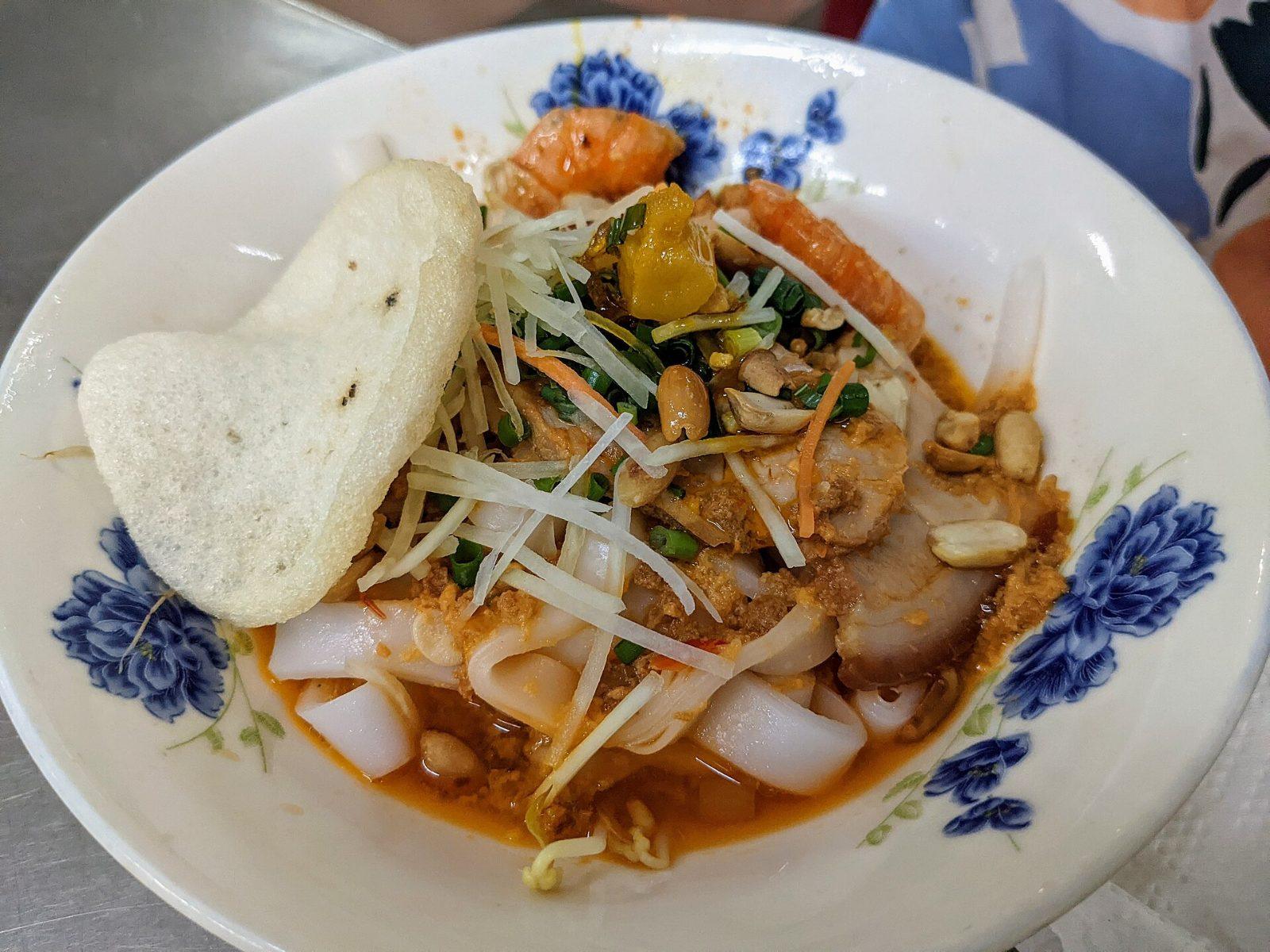 A bowl of mi quang, Vietnam's turmeric noodle dish, topped with shrimp, pork, peanuts, and a crispy rice cracker