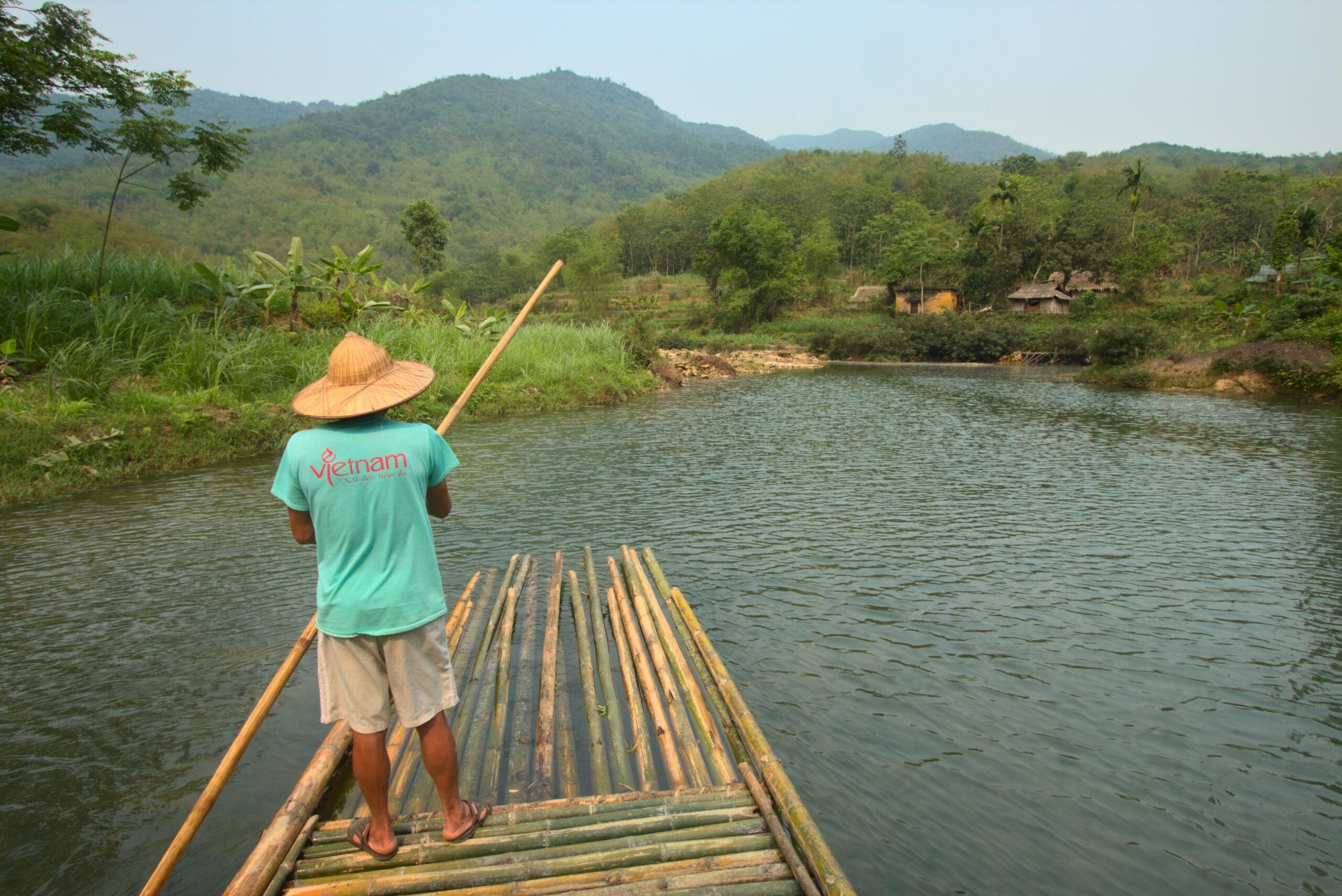 A local guide poling a bamboo raft along a river in Pu Luong Nature Reserve