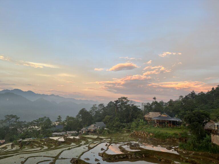 Sunset over flooded rice terraces and a thatched-roof ecolodge in Pu Luong