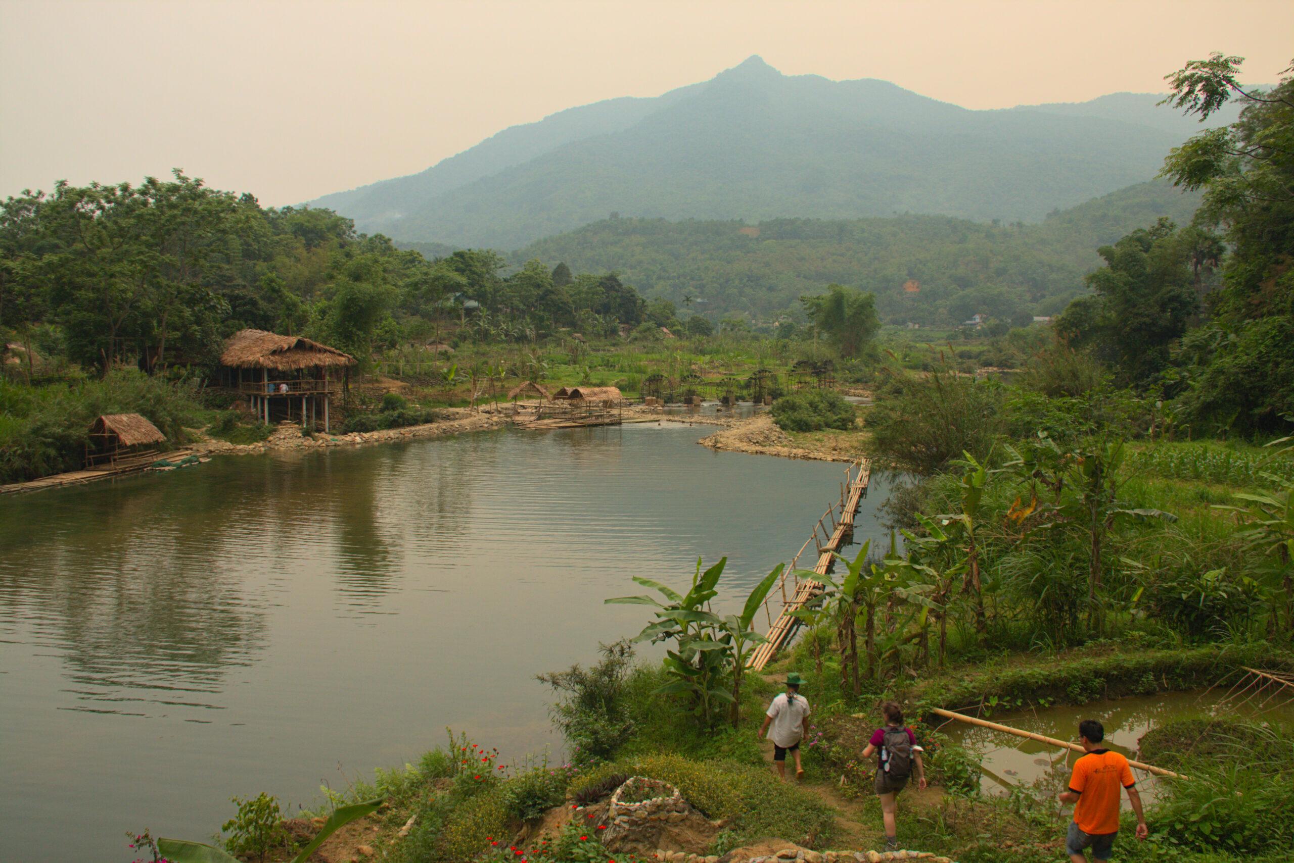 Trekkers walking beside a river toward a homestay in Pu Luong Nature Reserve