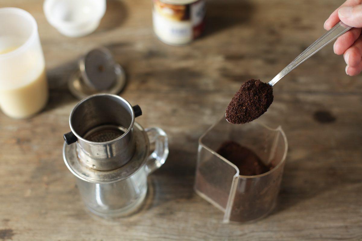 Scooping ground coffee into a traditional Vietnamese phin metal drip filter